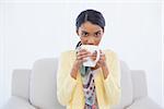 Young pretty woman sitting on sofa in bright living room drinking coffee