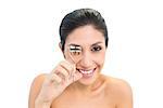 Brunette using eyelash curler and smiling at camera on white background