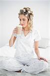 Peaceful pretty blonde wearing hair curlers smelling coffee sitting on cosy bed