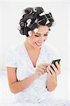 Pretty brunette in hair rollers using smartphone on bed at home in bedroom