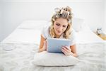 Peaceful pretty blonde wearing hair curlers using tablet pc lying on bed