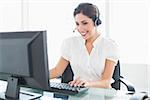 Cheerful call centre agent working at her desk on a call in her office