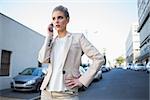 Serious elegant businesswoman on the phone outdoors on urban background