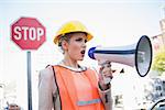 Businesswoman wearing builders clothes shouting in megaphone outdoors on urban background