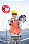 Businesswoman wearing builders clothes pointing at camera outdoors on urban background