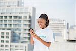 Smiling volunteer holding her mobile phone outdoors on urban background