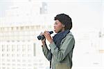 Curious casual model holding binoculars outdoors on a sunny day