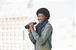 Smiling casual model holding binoculars outdoors on a sunny day