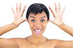 Joyful black haired woman posing with tongue out and hands around her head on white background