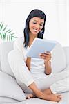 Relaxed black haired woman in white clothes using a tablet pc in a living room