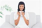 Stylish black haired woman in white clothes enjoying coffee in a living room