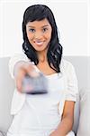 Cute black haired woman in white clothes changing tv channel in a living room