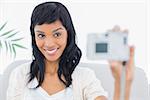 Natural black haired woman in white clothes taking a picture of herself in a living room