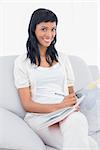 Cute black haired woman in white clothes writing on a notebook in a living room