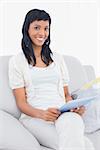 Lovely black haired woman in white clothes holding a tablet pc in a living room