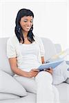 Thoughtful black haired woman in white clothes holding a tablet pc in a living room