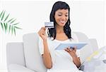 Lovely black haired woman buying online with her tablet pc in a living room