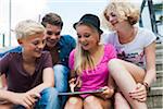 Group of teenagers sitting on stairs outdoors, looking at tablet computer, Germany