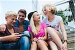 Group of teenagers sitting on stairs outdoors, looking at tablet computer, Germany