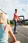 Backview of teenage girl in foreground and teenage boy on skateboard in background, Germany