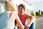 Teenage girl and teenage boy sitting on street, talking, Germany