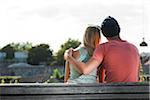 Backview of teenage boy with arm around teenage girl, sitting on bench outdoors, Germany