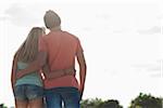 Backview of teenage boy and teenage girl with arms around each other, standing outdoors, Germany