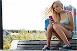 Teenage girl sitting on bench outdoors, looking at cell phone, Germany