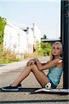 Portrait of teenage girl outdoors with skateboard, looking into the distance, sitting on street, Germany