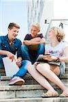 Teenagers sitting on stairs outdoors, talking and looking at tablet computer, Germany