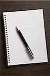 Close-up of blank notebook and writing pen on wooden background