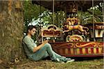 Young Man using Cell Phone while Sitting near Carousel, Mannheim, Baden-Wurttemberg, Germany