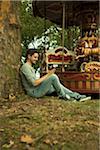 Young Man using Cell Phone while Sitting near Carousel, Mannheim, Baden-Wurttemberg, Germany