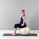 Portrait of young pregnant woman sitting on fitness ball,  studio shot