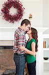 Happy young couple kissing in front of fireplace with Christmas decoration