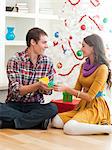 Young couple sitting under Christmas tree, opening Christmas present