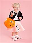 Baby girl (12-17 months) in 1950s style costume, holding pumpkin lantern for Halloween