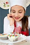 Little girl with chef's hat looking at muffins, Munich, Bavaria, Germany