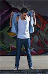 Young man standing in front of graffiti wall, Munich, Bavaria, Germany