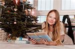 Woman with blond hair holding gift box next to Christmas tree, Munich, Bavaria, Germany