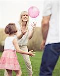 Father mother and daughter throwing ball to each other in the park