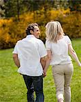 Couple holding hands with back to camera running through park