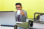 Portrait of Indian Businessman holding mug and working on his laptop computer at his desk