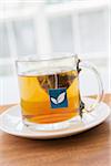 Cup of Tea in Clear Mug with Pyramid Tea Bag and Blue Tag on Wooden Tray, Studio Shot