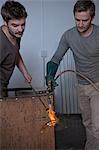 Two men heating glass in factory