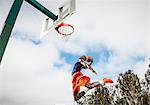 Young man jumping to score hoop in basketball