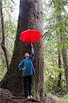 Mature woman holding red umbrella in forest