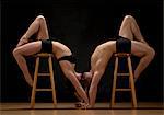 Mid adult dancers bending over stools against black background