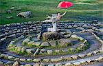 Mid adult dancers performing with red umbrellas in stone circle