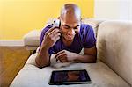 Mid adult male on sofa using digital tablet and smartphone